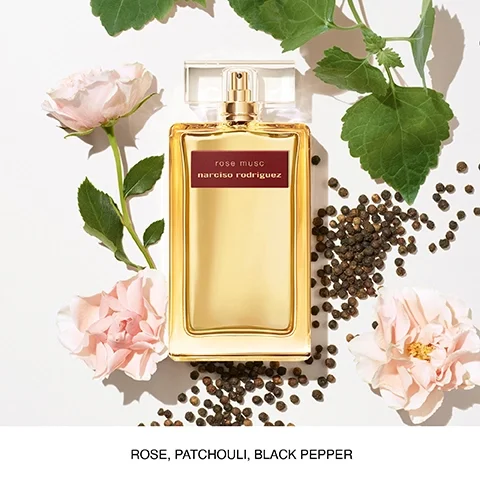 A bottle of rose musc perfume by Narciso Rodriguez is surrounded by pink roses, green leaves, and black peppercorns with the text rose, patchouli, black pepper below.