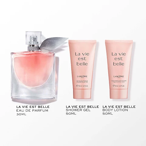 Image 2 - A Lancôme La Vie Est Belle fragrance set is displayed, featuring a perfume bottle with pink liquid and a silver ribbon, a light pink shower gel tube, and a light pink body lotion tube; visible text includes La vie est belle, LANCOME PARIS, Gel Douche Parfumé Scented Shower Gel, Lait de Parfum pour le Corps Fragrance-Body Lotion, e 50 ml 1.6 FL.OZ., LA VIE EST BELLE EAU DE PARFUM 30ML, LA VIE EST BELLE SHOWER GEL 50ML, and LA VIE EST BELLE BODY LOTION 50ML. Image 3 - A clear glass perfume bottle with pink liquid and a silver-sparkle band around its neck, adorned with a light blue ribbon, is surrounded by white flower petals, vanilla bean pods, and green leaves, with text labels reading IRIS, WARM VANILLA, SPUN SUGAR, EARTHY PATCHOULI. Image 4 - A pink Lancome perfume bottle with a clear cap and silver ribbon rests on a festive pink box decorated with gold and black clock face and winter wonderland illustrations, with the text LANCOME PARIS, Since 1935, and LANCOME EXPRESS visible on the box, and the overlay text OUR FIRST TASTY IRIS FRAGRANCE. Image 5 - Three Lancôme perfume bottles in shades of pink and red are displayed among multiple pink gift boxes adorned with clock-face designs and festive illustrations of Parisian landmarks and a train, set against a backdrop of pink curtains and a window revealing a soft sky and distant mountains, with visible text that reads SHOP THE COLLECTION, NEW VANILLE NUDE, LORIGINAL EAU DE PARFUM, LANCOME PARIS, Gift the extraordinary, LELIXIR EAU DE PARFUM.